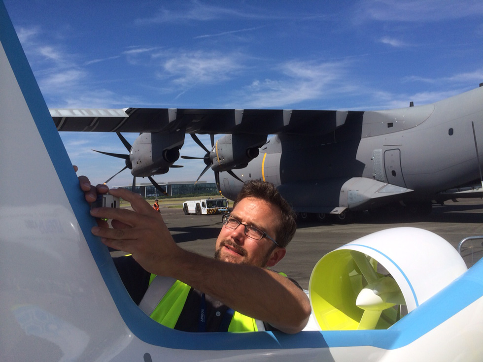 Tim Marquardt steht auf dem Rollfeld direkt an einem Flugzeug und befestigt eine Go-Pro. Im Hintergrund steht die A400M von Airbus.