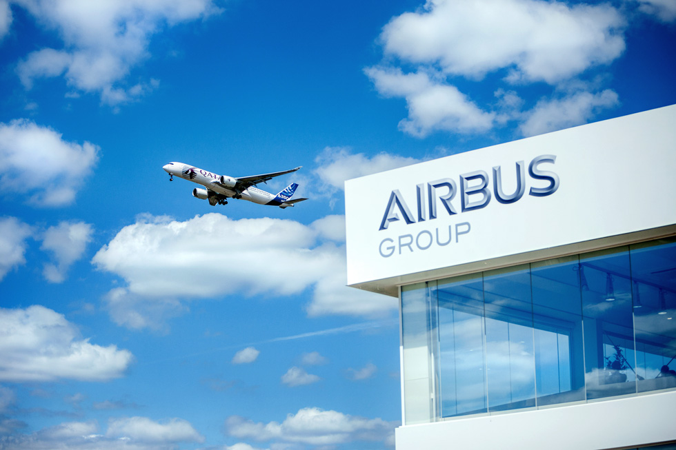 Blick in den Himmel zu einem Flugzeug. Rechts ist die obere Ecke eines Gebäudes mit der Aufschrift Airbus Group zu sehen.