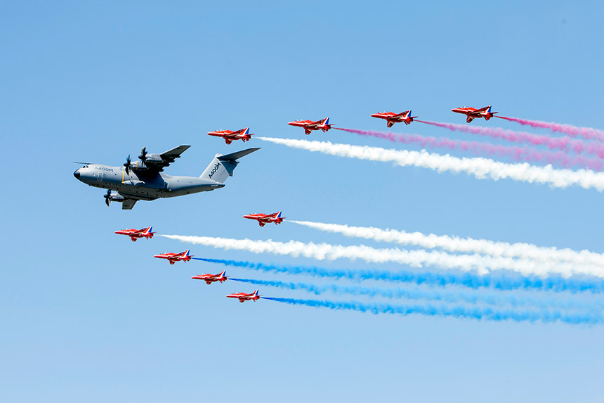 Airbus A400M fliegt mit Red Arrows in Formation am Himmel während Flugshow.