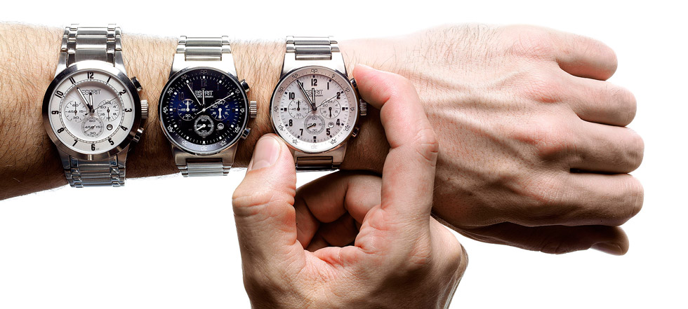 Ein Unterarm kommt von links ins Bild un d trägt 3 Armbanduhren. Eine weitere Hand  kommt von unten ins Bild un umfasst mit 2 Fingern die rechte Uhr.