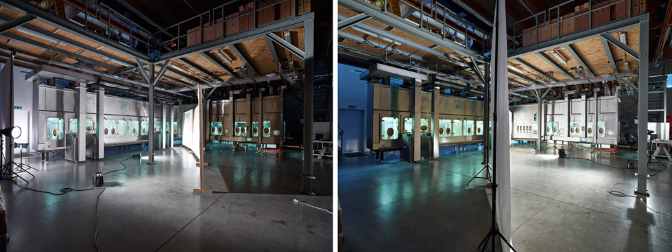 Eine große Halle in der eine Maschine aus Edelstahl steht. Eine weiße Trennwand und Blitzlampen stehen vor einem Teil der Maschine.