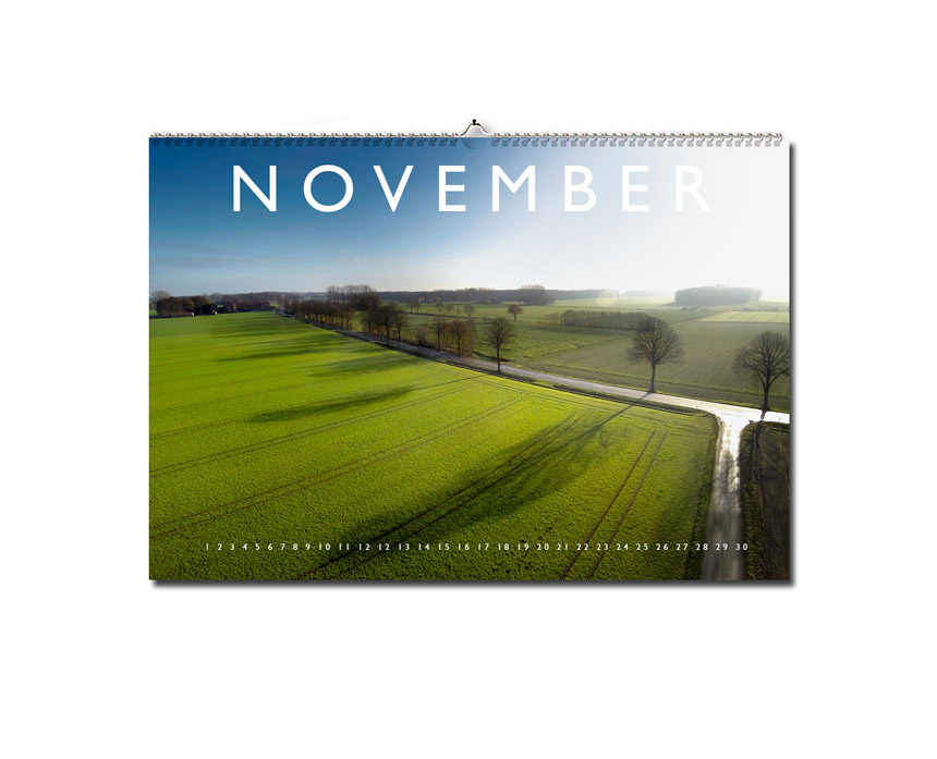 Luftaufnahme eines Feldes mit Bäumen am Straßenrand. Die Sonne scheint von rechts ins Bild und das Kalendarium von November ist zu lesen.