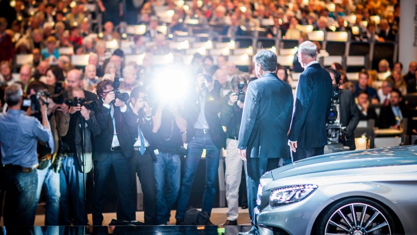 2 Männer, die vor einem Mercedes Auto stehen werden von vielen Pressefotografen abgelichtet.