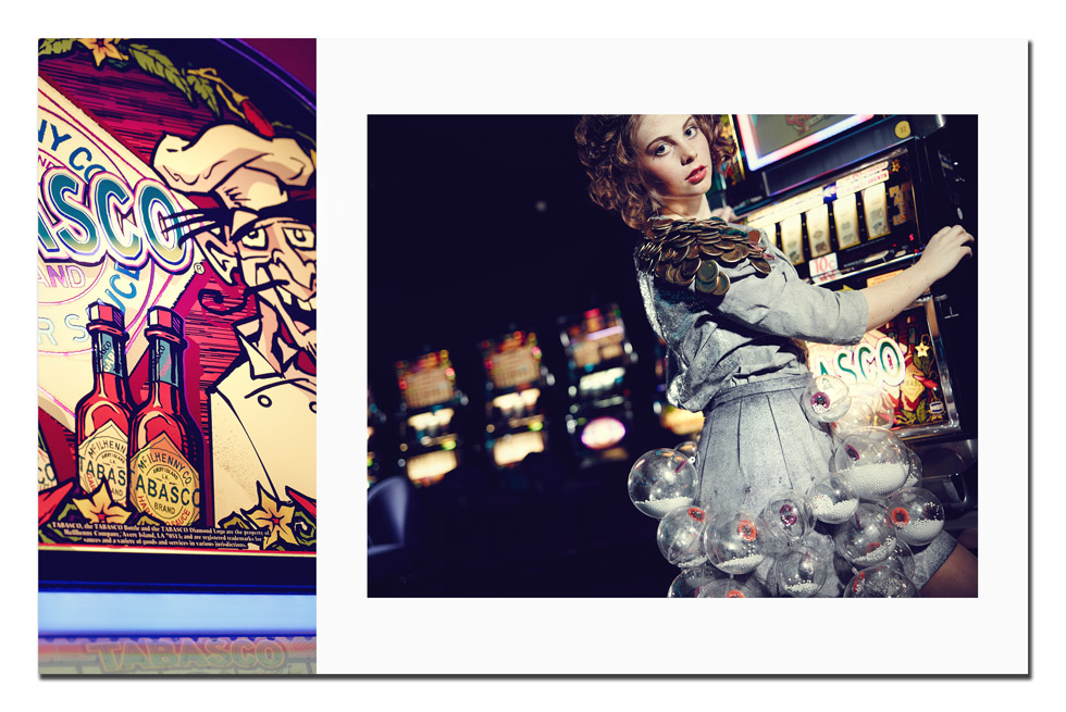 Eine Frau mit lockigen mittellangen haar steht an einer Slotmaschine im Casino. Ihr Kleid ist hellgrau und mit Jetons verziert.