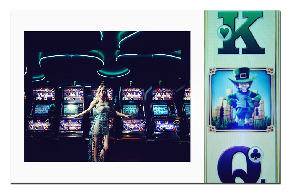 Eine Dame steht in an einem Casino vor einer Reihe Slotmaschines. Sie lehnt sich mit Ihren Armen an die Maschinen hinter ihr. Ihr Kleid ist mit Jetons verziert.