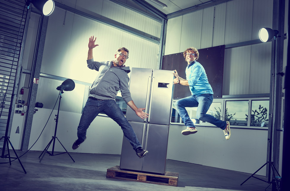 Tim und Sven Marquardt springen in die Luft neben einem Kühlschrank.