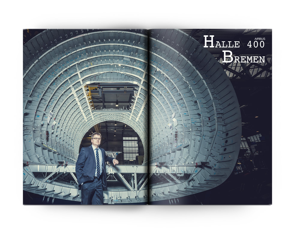 Aufgeschlagene Zeitschrift mit einem vollflächigem Foto eines Mannes der vor einem Flugzeug Rohbau steht.