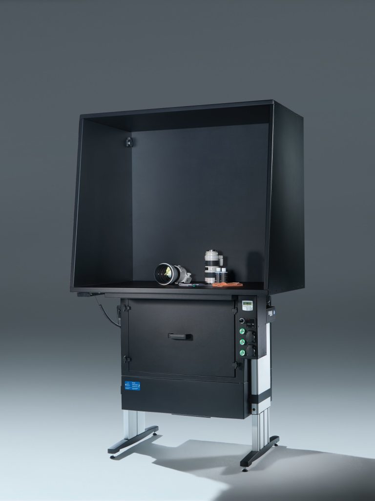 Schwarzer Absaugtisch von Böcker Filtertechnik, auf der Arbeitsfläche zwei weiße Teleobjektive und Reinigungszubehör, vor grauem Studiohintergrund