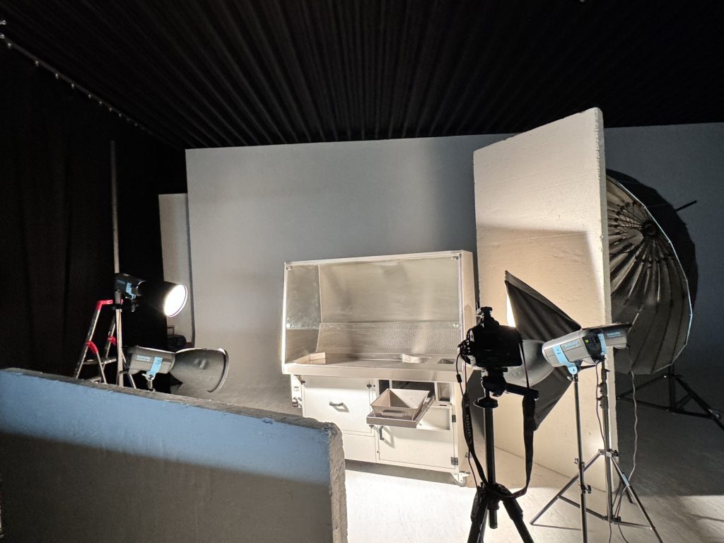 Fotoset im Studio mit Absaugtisch, großer Styroporplatte als Aufheller, Kamera auf Stativ und Schirm