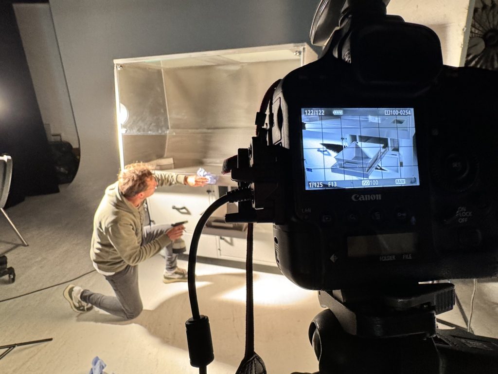 Fotograf kniet vor dem Absaugtisch und reinigt die Glasflächen, im Vordergrund das Kameradisplay mit der Vorschau